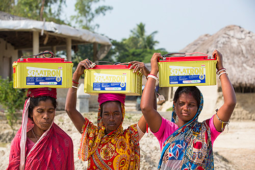 Women carrying batteries home from the solar power charging station